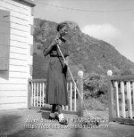 Huishoudster van de pasangrahan in he Bottom, Saba; Een huishoudster van het ambtenaren gastenverblijf maakt de veranda schoon (Collectie Wereldmuseum, TM-10021128)