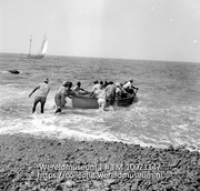 Passagiers worden van Saba naar een op de reede liggend schip gebracht; Een roeiboot wordt van het stenenstrand afgeduwd om passagiers naar het verder in zee gelegen schip te brengen (Collectie Wereldmuseum, TM-10021147)