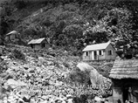 Saba. Negerwoningen tegen berghelling met Mangifera en Araceae; Kleien houten huisjes tegen een rotsachtige beghelling op Saba (Collectie Wereldmuseum, TM-10021157)
