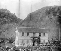 Saba. Huis van den Gezaghebber; Een ambtswoning met gehezen wapperende vlag omringd door rotsen (Collectie Wereldmuseum, TM-10021318)