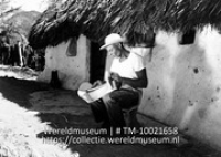 Koenoekoe-huisje, Curacao. De man ervoor is bezig een zadel te maken; Een man tijdens de vervaardiging van een zadel in de schaduw van een kunukuhuis (Collectie Wereldmuseum, TM-10021658)