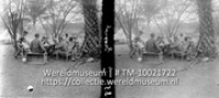 Curacao 1930. Eetpartij in kamp Savonet met gasten vam de C.P.I.M rechts stam van dadelpalm, links mimosaboom; Een groep mannen aan tafel onder een dadelpalm (Collectie Wereldmuseum, TM-10021722)