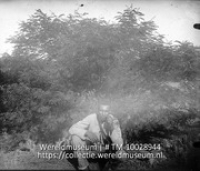 Vegetatie der W-Ind. eil. Acacia-struikvegetatie; Een man zit gehurkt voor een Acacia struik; A man squatted in front of a acacia bush (Collectie Wereldmuseum, TM-10028944)