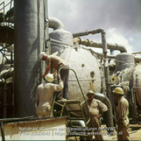 Arbeiders aan het werk op Lago olieraffinaderij bij de destillatieketels (Collectie Wereldculturen, TM-20029543), Lawson, Boy (1925-1992)