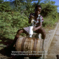 Het vullen van een fles met zoet water uit de ton; Een jongetje vult zijn tonnetje met zoet water uit een tap, welke in verbinding staat met een windpomp. (Collectie Wereldmuseum, TM-20030096), Lawson, Boy