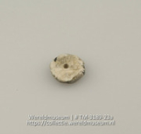 Schijf van schelp met 2 gaatjes, vermoedelijk een knoop of kraal (Collectie Wereldmuseum, TM-3189-23a)