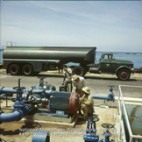 Arbeiders aan het werk met een aggregaat en een tankwagen op Lago olieraffinaderij aan zee (Collectie Wereldculturen, TM-20029555), Lawson, Boy (1925-1992)